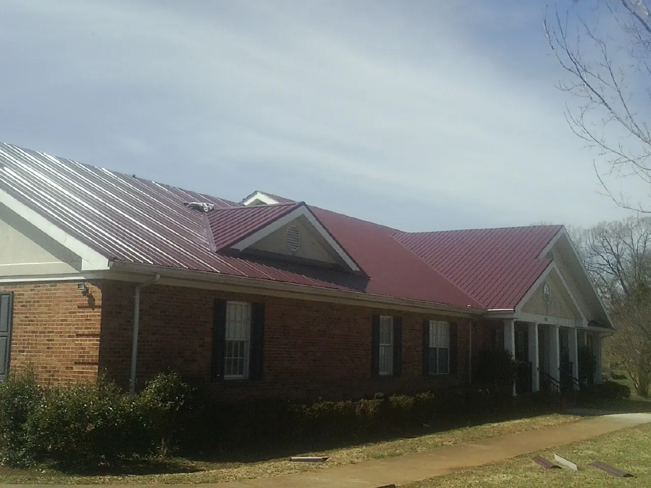 Red metal roof with gabled entries on a long brick building, from a Hail Damage Roof Repair job in Orofino