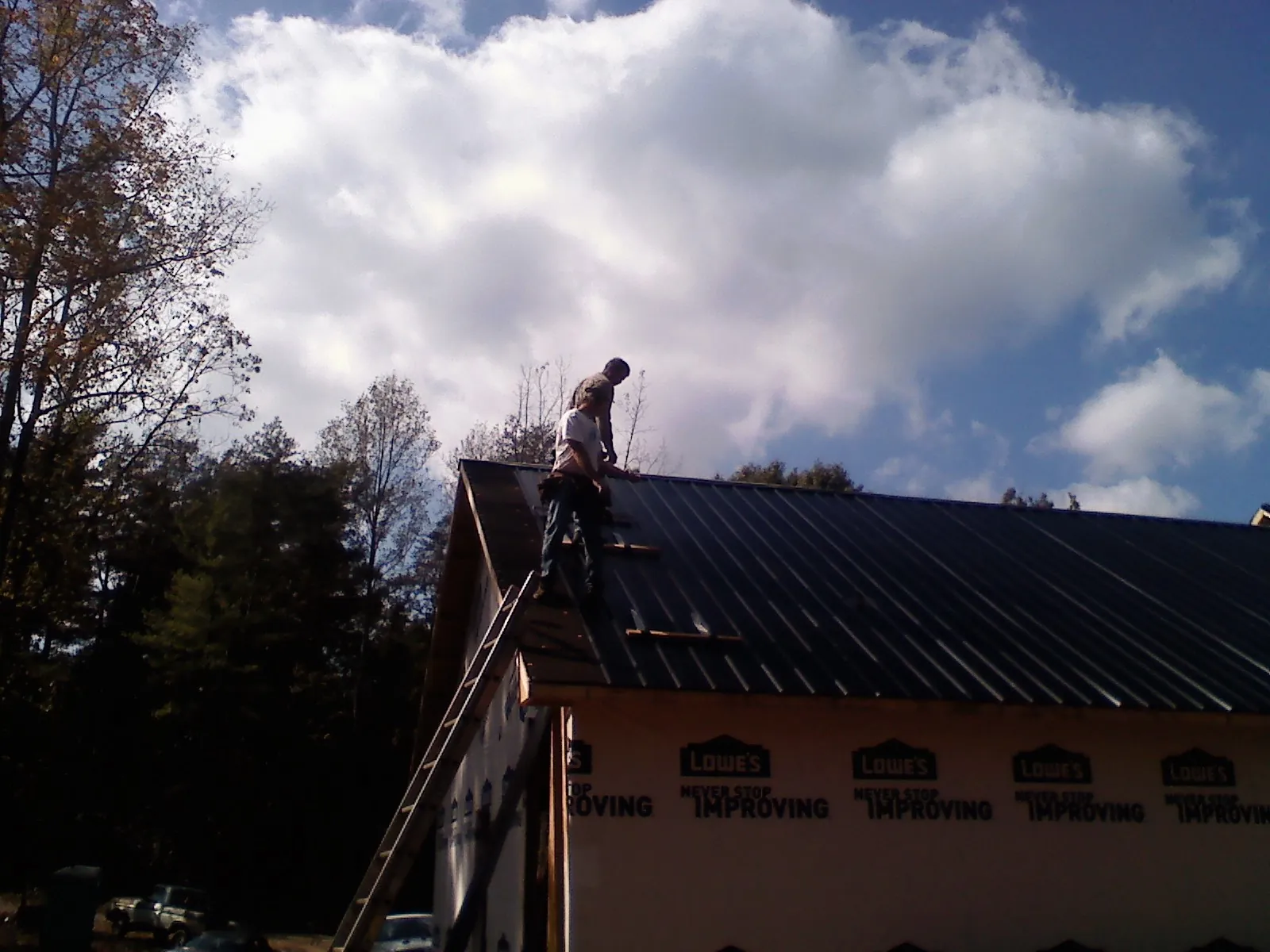 Roofer fastening dark metal panels high against a cloudy sky, from a Roof Inspection job in Orofino