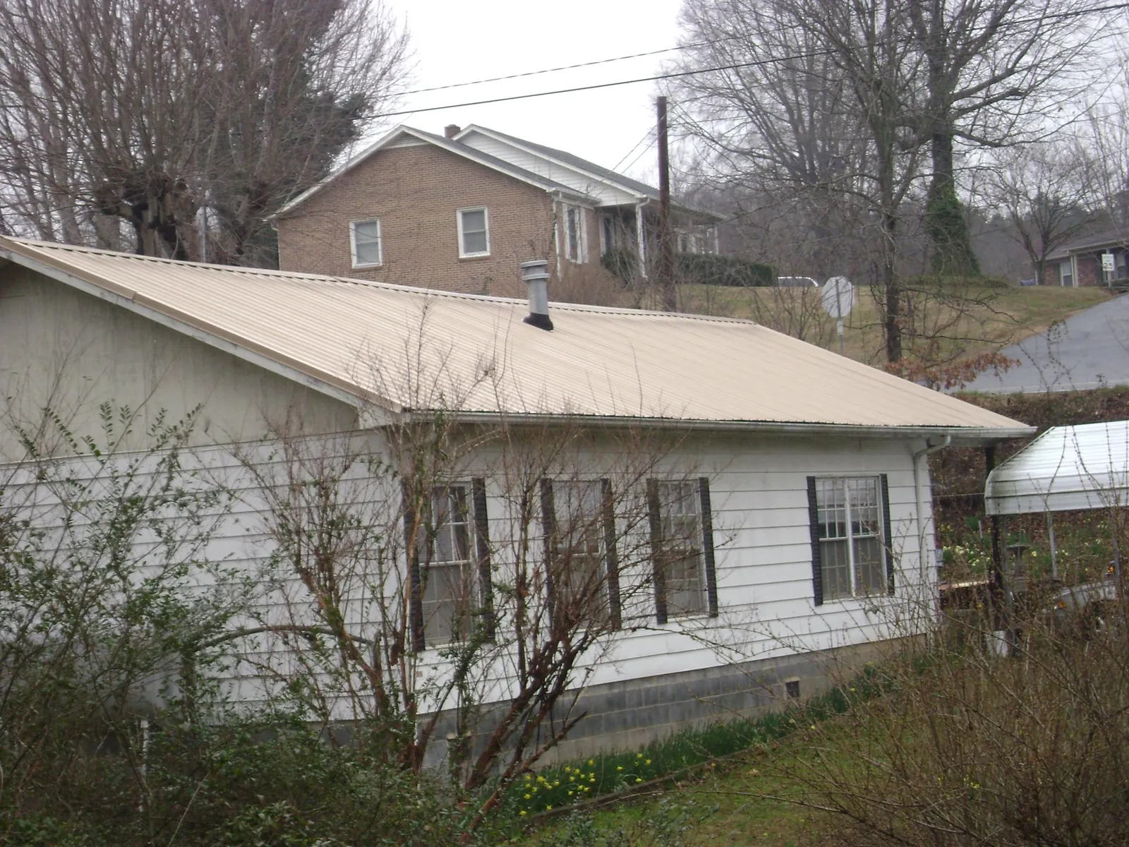 Tan metal roof on a white sided house set into a hillside — Commercial Roofing by Roofing Brothers in Orofino
